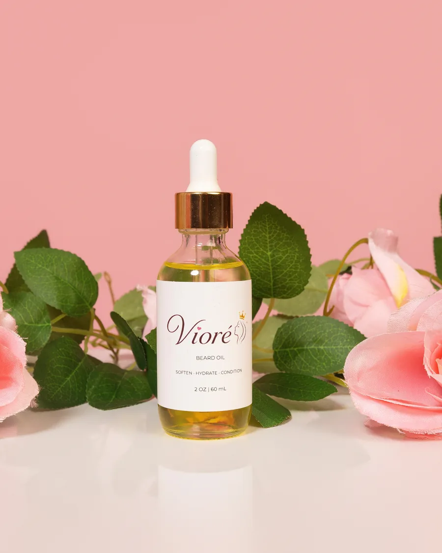 Vioré Beard Oil, a 2 oz glass dropper bottle with a gold cap, standing among pink roses