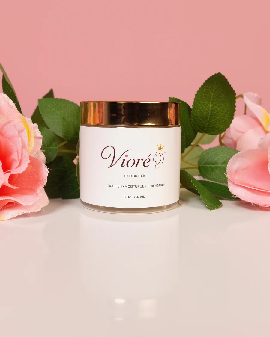Vioré Hair Butter, an 8 oz jar with a gold lid, standing among pink roses